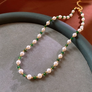 Close-up of pearl necklace with green faceted beads and gold accents on a display tray