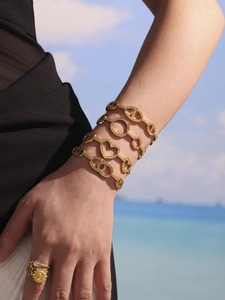 Detail of layered gold zircon bracelets and rings on a model with a beach backdrop
