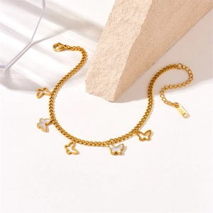 Detailed view of gold butterfly anklet with white shell inlays on a textured stone