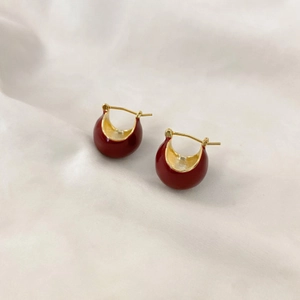 Détail de créoles en forme de U émaillées rouges avec métal doré sur tissu beige plissé