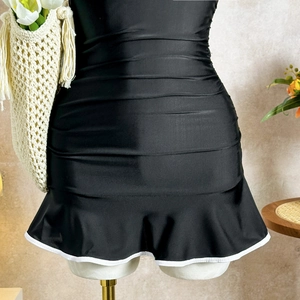 Detail of ruched black swimsuit featuring white contrast trim and ruffled hemline