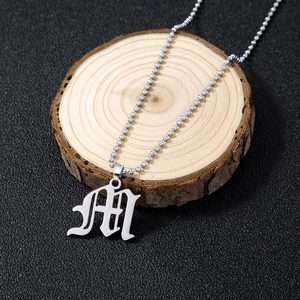 Close-up of silver gothic M letter pendant on bead chain against dark textured background
