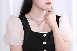 Detail of a layered silver necklace featuring a minimalist hollow pendant on a model