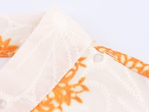 Dettaglio macro dello scollo a V con stampa floreale arancione e ricami su tessuto bianco