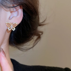 Close-up of a gold butterfly stud earring with white zircons worn on an earlobe