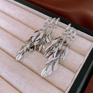 Detailed macro view of silver layered leaf tassel earrings in a beige velvet jewelry box
