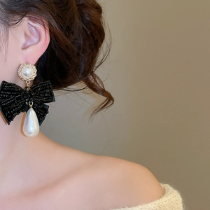 Detail of elegant oversized bow earrings with drop pearls on model ear