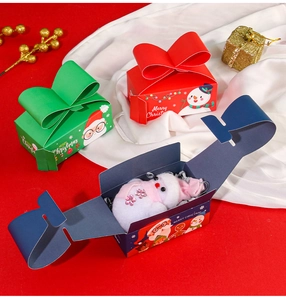 Opened Christmas gift box with bow design showing small plush toy inside for holiday favors