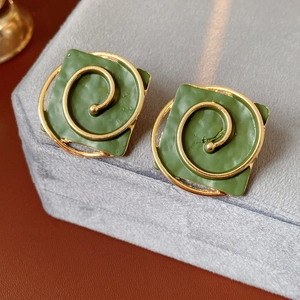Close-up of vintage green square earrings with golden spiral metal design on velvet