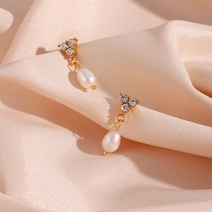 Close-up of gold stainless steel pearl earrings with three rhinestones on silk
