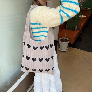 Shoulder view of light brown knitted heart tote bag with black patterns and woven texture