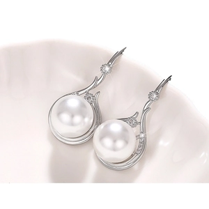 Elegant white pearl drop earrings with sparkling diamonds on a white ceramic plate
