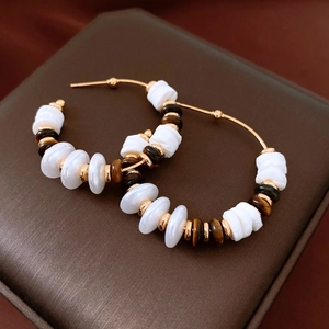 Détail de créoles plaquées or 18 carats avec perles blanches et œil de tigre