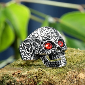Macro detail of silver skull ring featuring floral engravings and red gemstone eyes