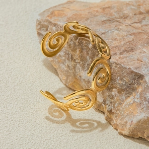 Detail of gold hollow spiral pattern open bangle displayed on a textured stone