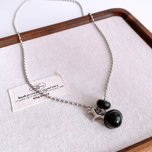 Detail of silver bead chain with black sphere pendants and pony charm on linen tray