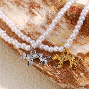 Close-up of pearl necklace featuring gold and silver hollow tiger pendants on wood