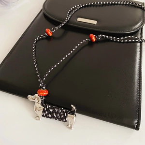 Macro view of woven dachshund puppy pendant with silver metal accents and orange beads