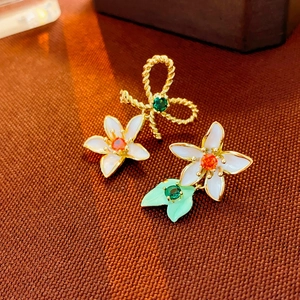 Detail view of asymmetric gold-plated flower and bow earrings with colorful enamel and gems
