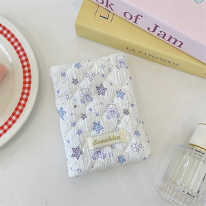 Close-up of quilted white passport case with purple teddy bear pattern and fabric label