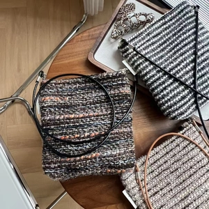 Three assorted striped tweed crossbody bags with long straps displayed on a wooden table