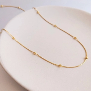 Macro shot of an elegant 18K gold-plated beaded snake chain necklace on white ceramic