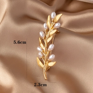 Macro detail of golden olive leaf brooch with pearls showing 5.6cm size on satin