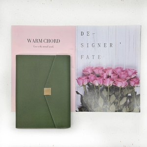 Close-up of a dark green notebook with litchi grain leather and a gold square buckle