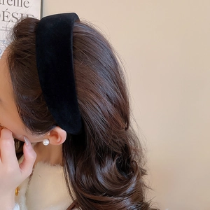 Detail view of a thick black velvet headband worn by a model with curly hair