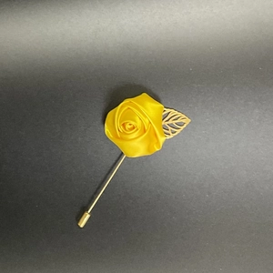 Macro detail of a handmade yellow satin rose lapel pin with a hollow golden leaf accessory