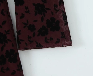 Detail of burgundy mesh fabric featuring black flocked floral pattern on long sleeve dress