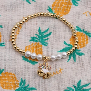 Détail d'un bracelet doré perlé avec perles factices et pendentif cloche serti de zircons