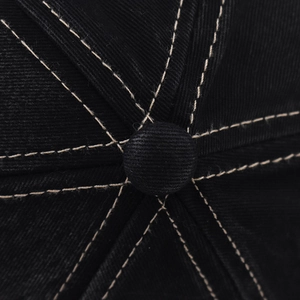 Detailed macro view of the top button and beige stitching on a black cotton baseball cap
