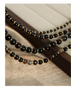 Macro detail of multi-layer necklace with black onyx beads and golden spacers on a tray