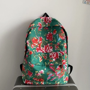 Detail view of the red and green floral print backpack resting on a grey suitcase