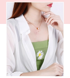 Detailopname van een gouden ketting met witte keramische hanger gedragen door een model