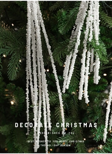 Close-up of white pearl bead sprig hanging on a Christmas tree with warm lights