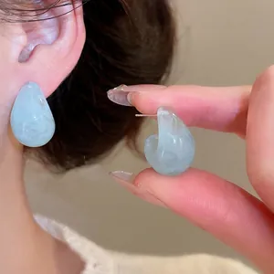 Light blue resin C-shaped drop earrings with marble texture on neutral background