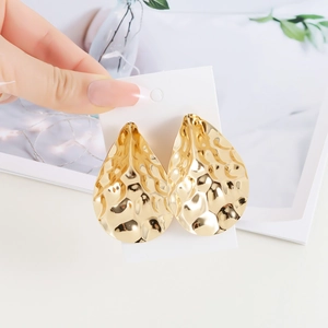 Detail of large golden water-drop earrings with a hammered metal texture on a card