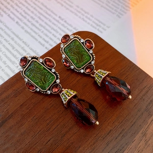 Detail of vintage baroque earrings with green inlay and red teardrop crystal on wood