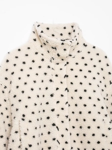 Détail du col d'une veste polaire à motifs d'étoiles noires sur simili mouton crème
