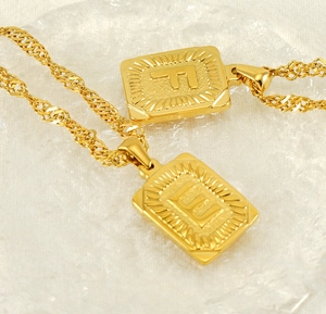 Close-up of 18K gold plated F and E square letter pendants on twisted chain over ice texture