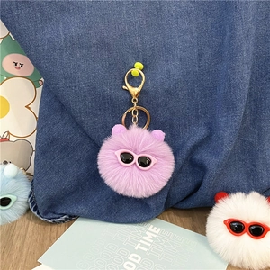 Close-up of a cute purple fuzzy pom-pom keychain ornament with tiny pink sunglasses