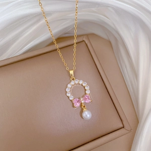 Macro detail of gold necklace with pink crystal bow and white pearl on satin