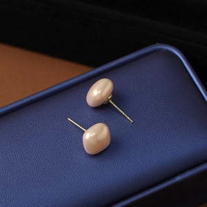 Macro view of geometric pink pearl stud earrings resting on a blue textured jewelry box