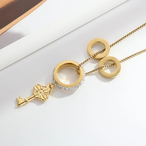 Detail of gold key pendant necklace featuring crystal-encrusted rings on a sleek long chain