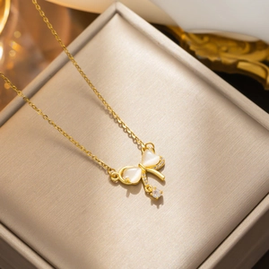 Elegant gold bow necklace with cat-eye stone pendant displayed in a beige jewelry box