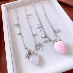 Detailed close-up of strawberry pendant necklaces with pearls on a white velvet jewelry tray