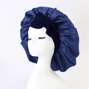 Detail of a navy blue satin silk sleep bonnet with a decorative bow on a mannequin