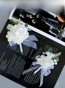 Close-up of artificial white rose boutonnieres with greenery and pearls on dark background